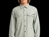 un homme vêtu d'une chemise grise et d'un chapeau noir, debout devant un fond noir