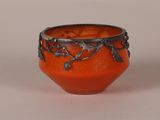 a small orange bowl with a metal decoration on it