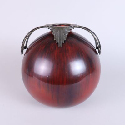 a red vase with a metal handle sitting on a white surface