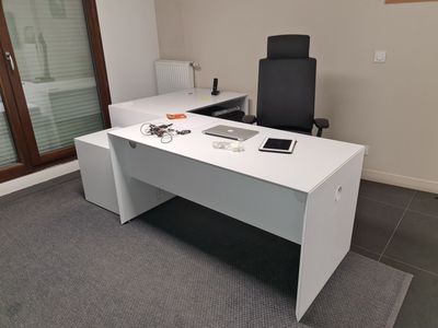 un bureau blanc avec une chaise noire et un ordinateur portable posé dessus