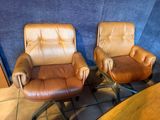 two brown leather chairs sitting next to each other on a tiled floor