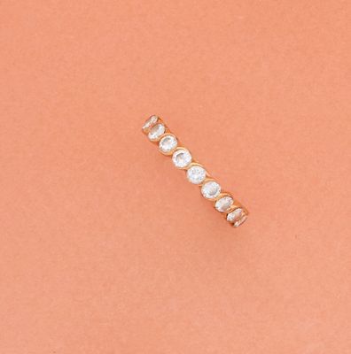 une bague simple en forme de barre, ornée d'une perle et d'un diamant, sur fond couleur pêche