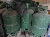 Plusieurs bouteilles de gaz vert sont empilées sur une palette dans un garage.