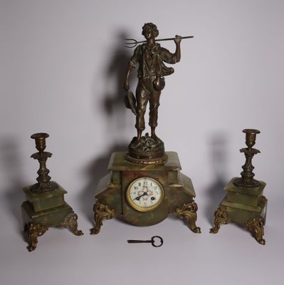 a clock with a statue on top of it next to three candles