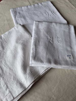 three white linen napkins with embroidered monograms on them on a bed