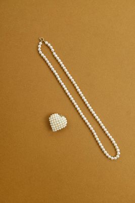 a white pearl necklace and a heart shaped broocher on a brown background