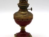 un vase rouge et doré posé sur un socle, sur une surface blanche