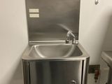 un lavabo en acier inoxydable dans des toilettes publiques, avec un distributeur de serviettes en papier fixé au mur