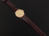 a gold watch with a brown leather strap on a black background