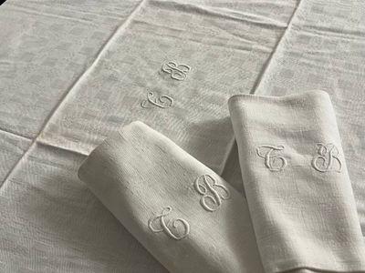 trois serviettes de table en lin blanc ornées de monogrammes, posées sur une table