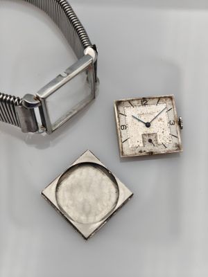 a silver watch and a square watch sitting on a table