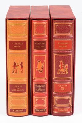 Trois livres sont posés sur une surface blanche ; l'un est rouge et l'autre est doré.