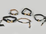 a set of five black leather wrist cuffs with brass hardware