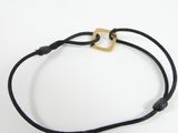 a close up of a black cord bracelet with a gold square on it