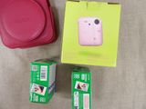 a pink camera sitting next to a pink case and a red bag