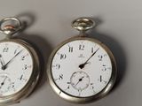 two silver pocket watches sitting side by side on a table