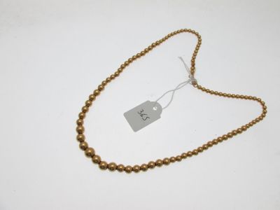 un gros plan sur un collier composé de perles dorées, orné d'une étiquette