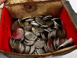 une boîte remplie de pièces argentées et rouges, vers laquelle une main se tend