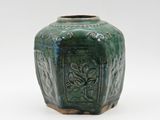 un vase vert posé sur une surface blanche, avec un fond blanc