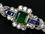 a close up of an emerald and sapphire broochle on a black surface