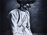 photographie en noir et blanc d'une femme portant un turban, assise sur un lit