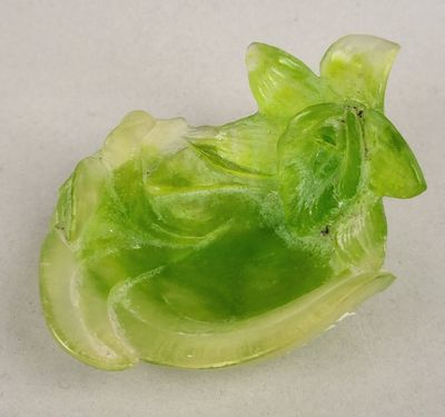 une figurine en verre vert représentant un oiseau posée sur une surface blanche