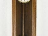 une horloge en bois accrochée au mur, à côté d'un mur blanc