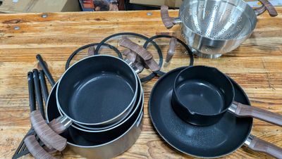 Plusieurs casseroles et poêles sont posées sur une table en bois.