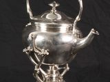 an antique silver tea kettle on a stand against a black background