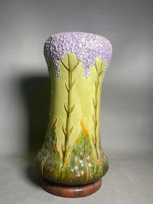a green vase with purple flowers on it sitting on a table