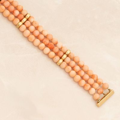 a close up of a peach beaded bracelet with a gold clasp