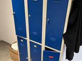 three blue lockers in a room with a black coat hanging on the wall