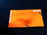 an orange folder with a sticker on it sitting on the hood of a car
