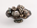 un bol en argent rempli d'objets décoratifs en argent, posé sur une surface blanche