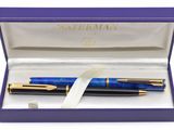un stylo bleu dans une boîte violette ornée d'un ruban blanc