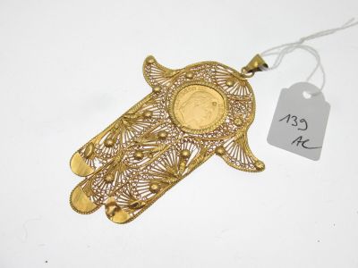 une photo d'un bijou en forme de main de Hamsa en or, sur lequel est apposée une étiquette de prix