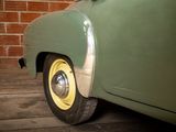 a green car with a yellow rim parked in front of a brick wall