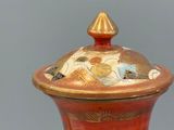 a red vase with a gold lid sitting on a table