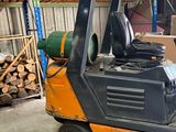 a forklift in a warehouse with a pile of wood in the background