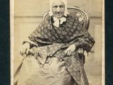 une vieille photo d'une femme assise sur une chaise, un foulard sur la tête