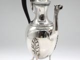 an antique silver coffee pot with a black handle on a stand