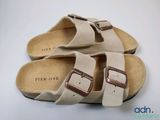 une paire de sandales beiges ornées de deux boucles, posées sur une surface blanche