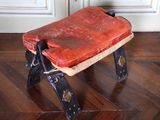 un petit tabouret avec une assise en cuir posé sur un sol en bois
