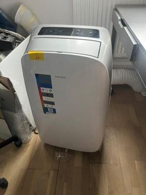 a white air conditioner sitting on the floor next to a desk