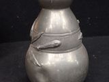 a silver vase with a bird on it on a black background
