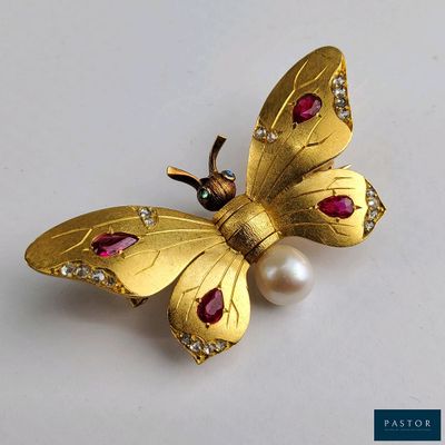 une image représentant une broche en forme de papillon en or ornée de perles, sur un fond blanc