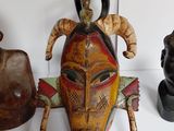 several african masks are displayed on a shelf above a busturine