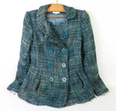une veste en tweed bleu avec des boutons bleus, suspendue à un cintre sur un mur blanc