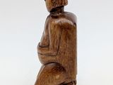 wooden figurine of a woman sitting on a stool with a hat on her head