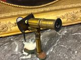 un télescope doré posé sur une table en marbre, à côté d'un miroir